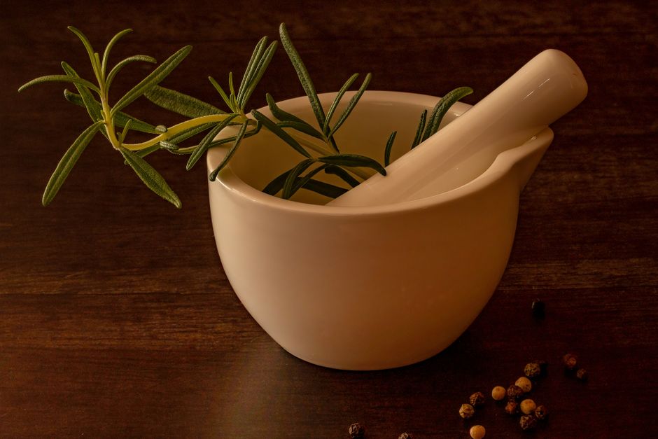 White porcelain mortar and pestle with rosemary on a wooden surface, ideal for culinary and herbal images.