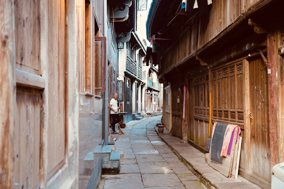 A narrow paved street with traditional wooden houses in an old rustic alleyway.