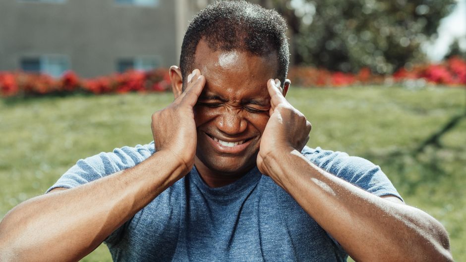 African American man massaging his temples outdoors, showing stress and emotion.