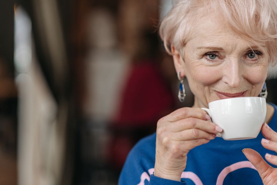 Close-up of a senior woman enjoying a hot drink, indoors, smiling warmly.