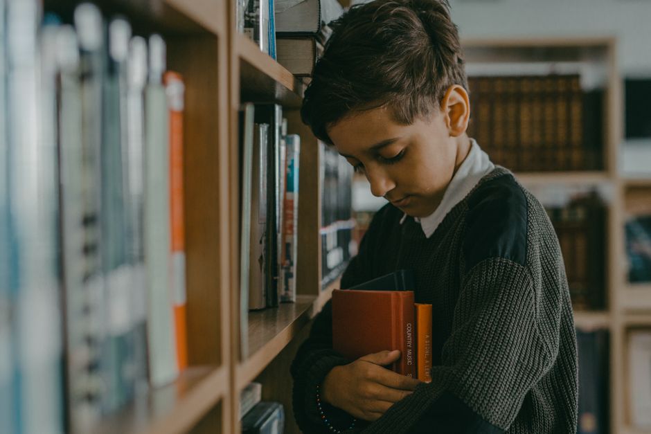 Young boy immersed in books at a cozy library, embracing learning.