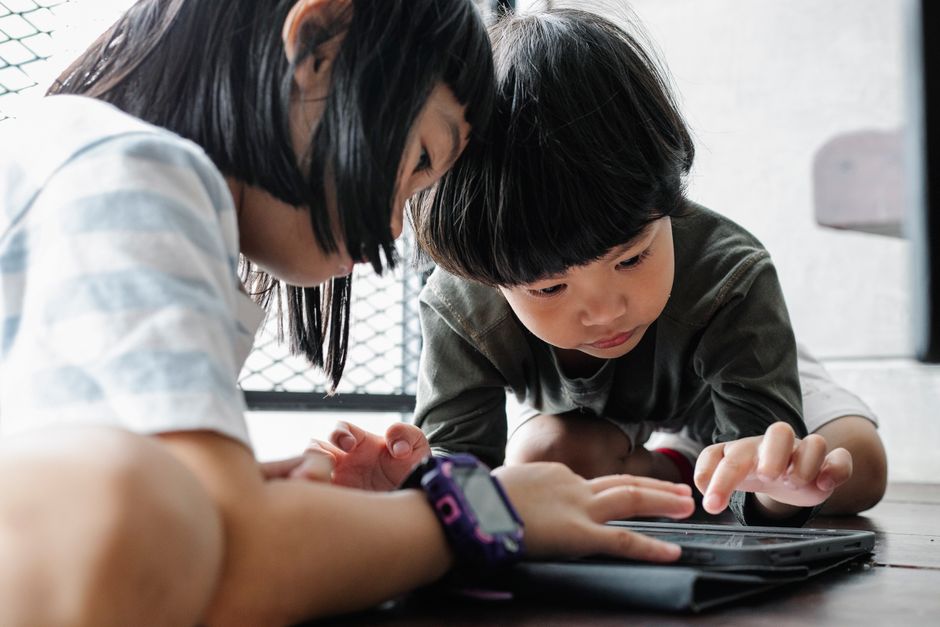 Two children focused on using a tablet indoors, engaging with technology for learning and play.