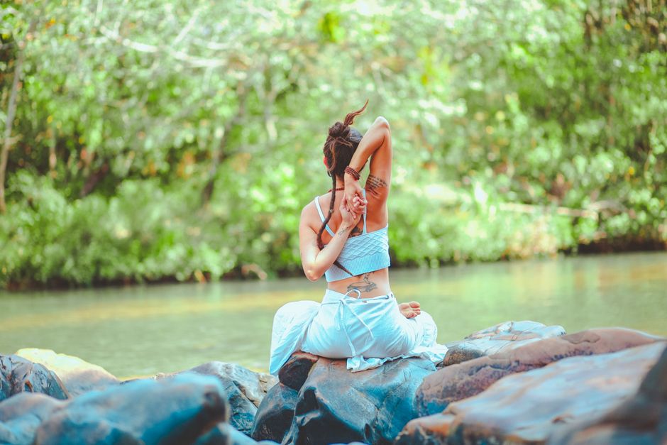 A woman practicing yoga on rocks by a serene river surrounded by lush greenery.