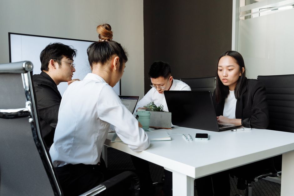 Group of business professionals collaborating during a meeting with laptops in a modern office setting.