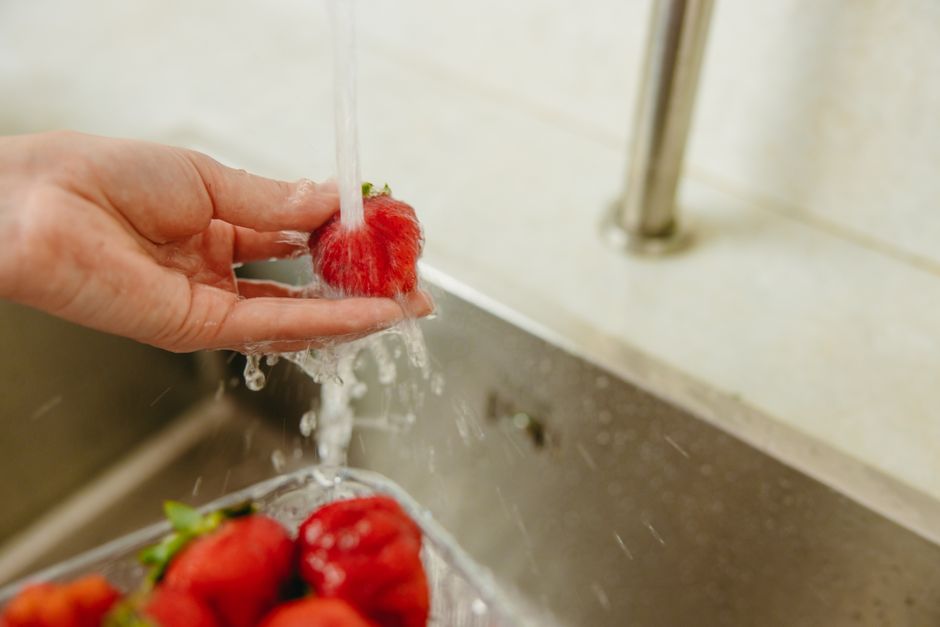 Close-up of a hand washing ripe strawberries under running water in a kitchen setting.