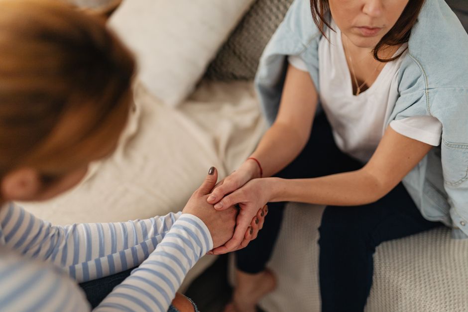 Close-up of two women holding hands on a sofa, expressing care and empathy.