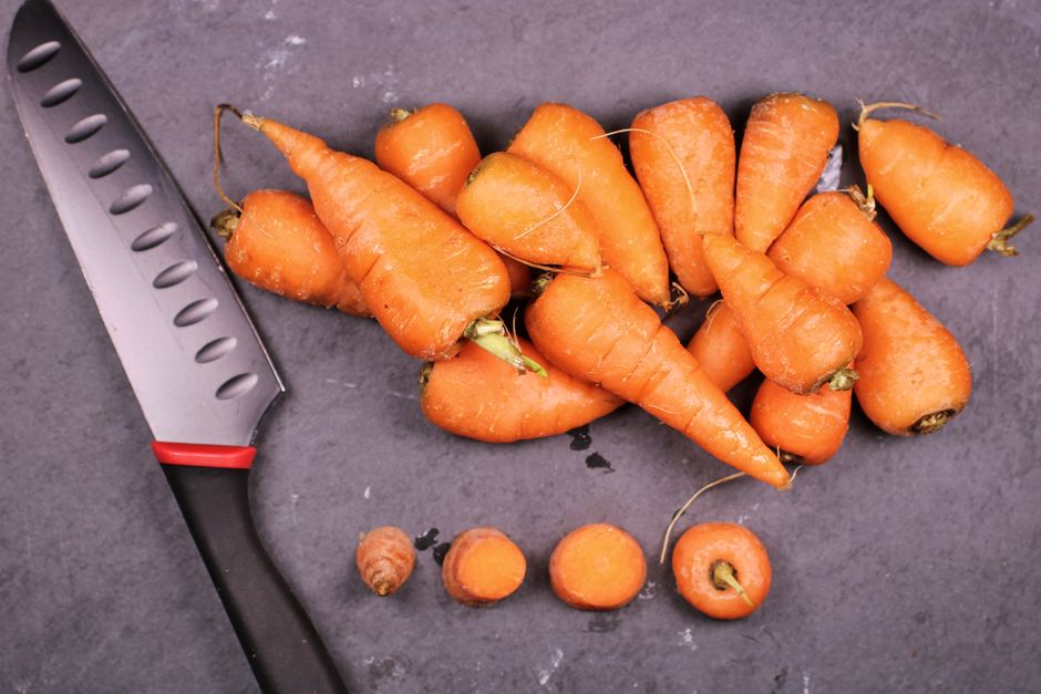 Freshly harvested carrots with a knife on a slate surface, perfect for cooking inspiration.