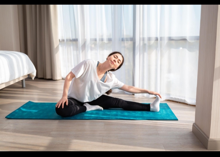 A woman practicing a gentle yoga stretch on a mat in a bright room, illustrating flexibility, physical fitness, and mental well-being.